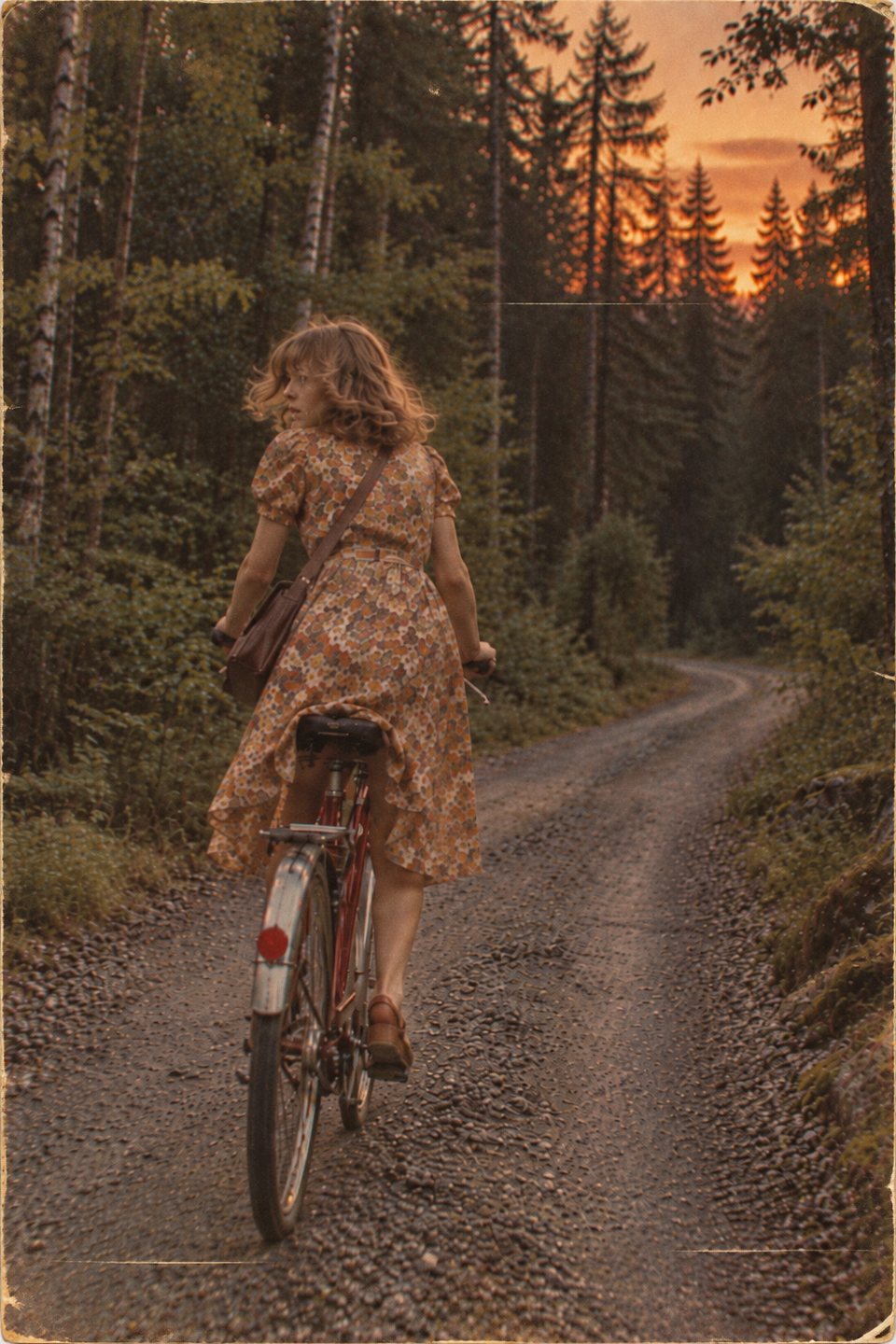 Ung kvinna på cykel på en skogsväg i solnedgången, med blicken över axeln
