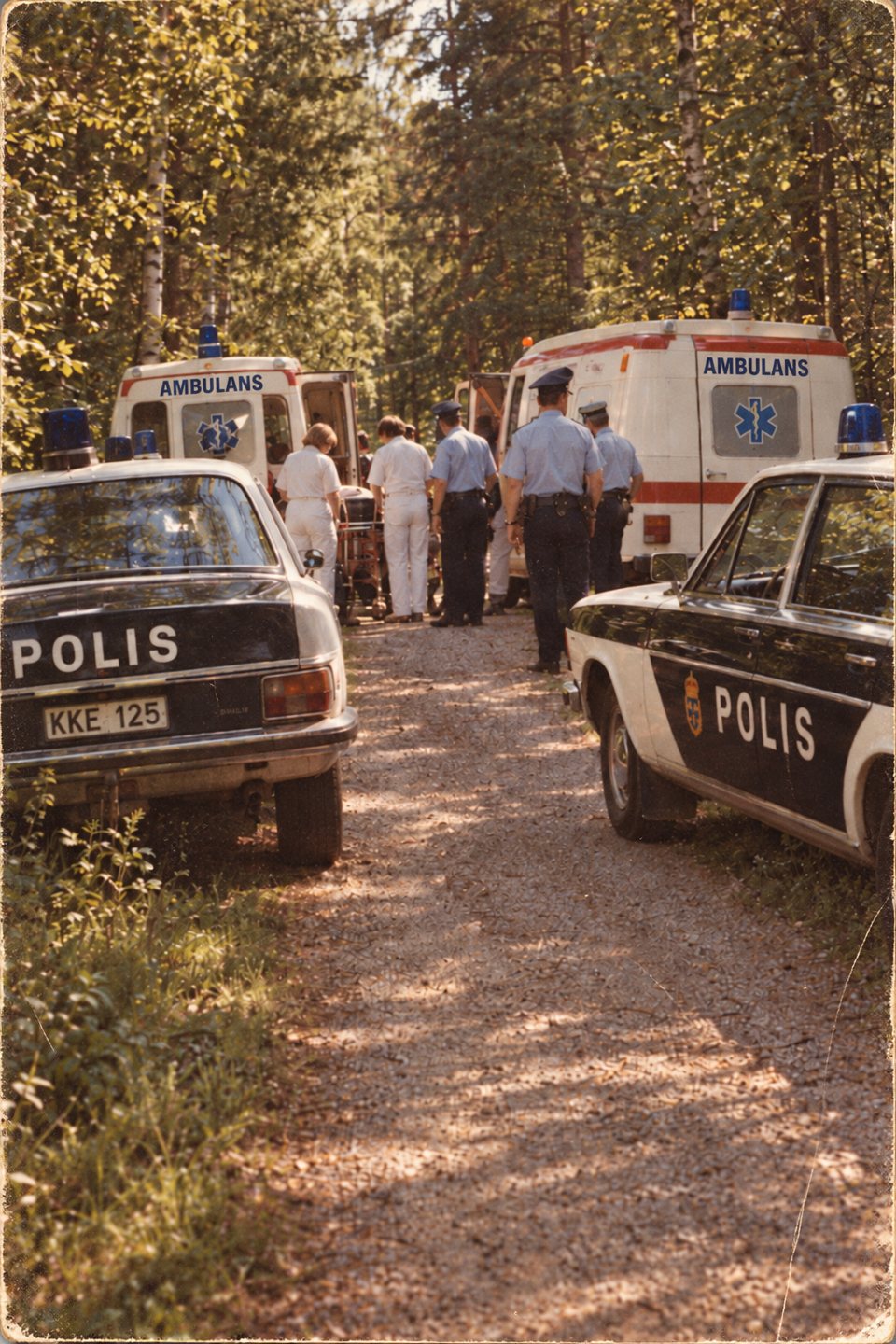 Polisbilar och ambulanser på en skogsväg, med poliser och ambulanspersonal
